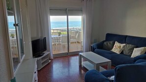 Un salon avec un canapé bleu, un téléviseur et un balcon donnant sur la mer.