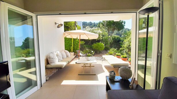 A modern patio with a sofa, a table, and an umbrella, overlooking a lush garden.