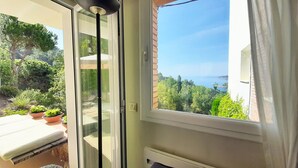 A balcony with a glass door, potted plants, and a view of a coastal landscape.