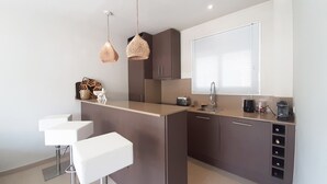 A modern kitchen with a central island, pendant lights, and a window with blinds.
