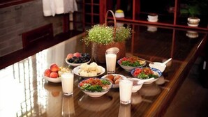 A breakfast table with various dishes, a basket with flowers, and a milk jug. - Yamingyuan Inn (Dali City)