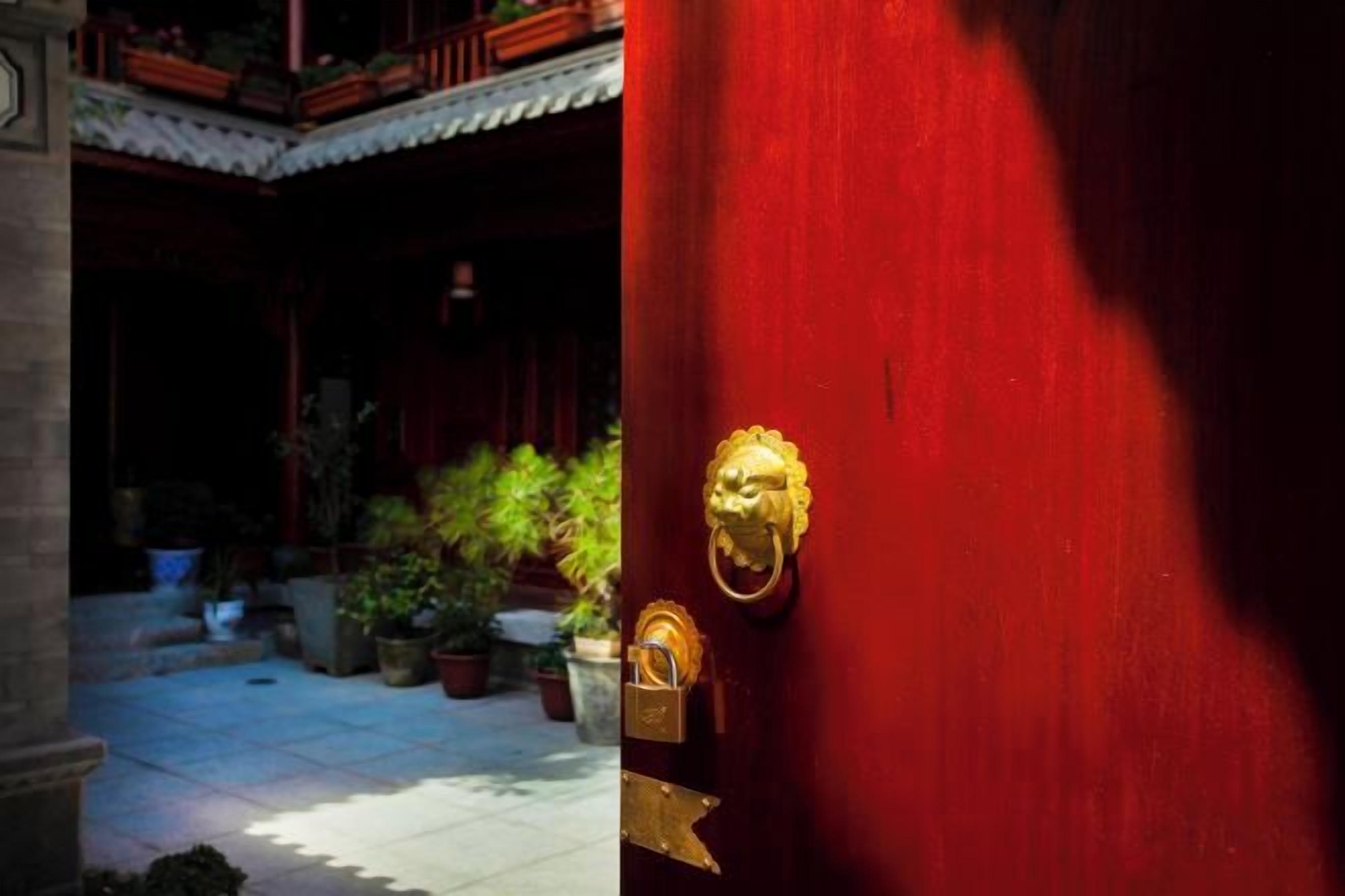 Una puerta roja con pomo dorado, un patio con plantas en macetas y un estilo arquitectónico tradicional.