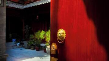 Una puerta roja con pomo dorado, un patio con plantas en macetas y un estilo arquitectónico tradicional.