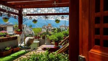 Un espacio exterior techado con una silla colgante, plantas en macetas y vistas a edificios y montañas.