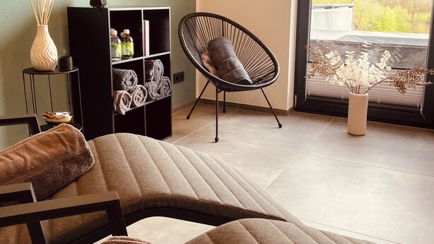 Una sala de estar moderna con un sofá, una silla, una estantería y vistas al exterior.