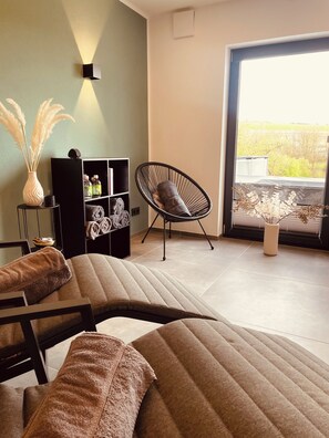 A modern living room with a sofa, a chair, a bookshelf, and a view of the outdoors.