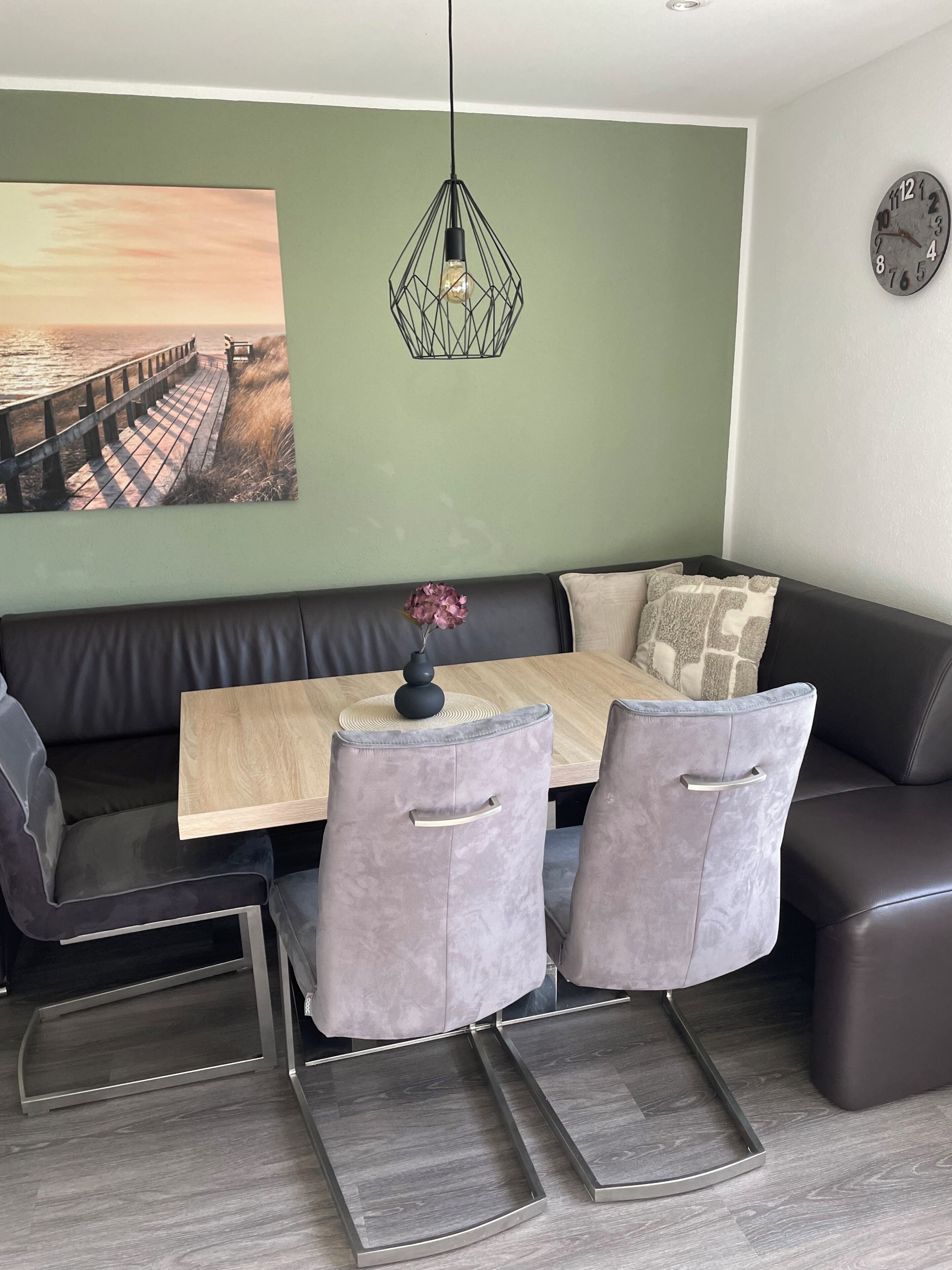 Un comedor moderno con una mesa de madera, sillas tapizadas de gris y una lámpara colgante.