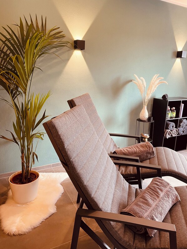 A modern lounge area with a cushioned chair, a potted plant, and a wall-mounted light fixture.