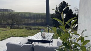 Un área de estar al aire libre con una mesa y sillas, rodeada de vegetación y vistas al campo.