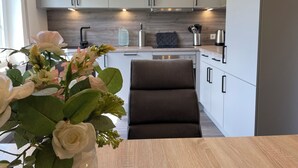 Una cocina moderna con armarios blancos, una silla marrón oscuro y un jarrón con flores.
