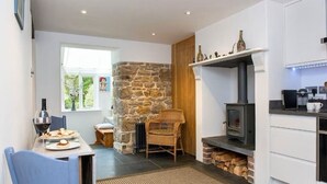 A cozy kitchen with a stone wall, a built-in wood stove, and a dining area with a table set for two.