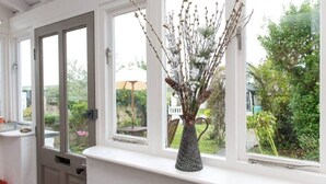 A room with a white window sill, a vase with branches, and a view of a garden.