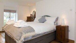 A neatly made bed with folded towels, a bedside lamp, and a wooden nightstand.