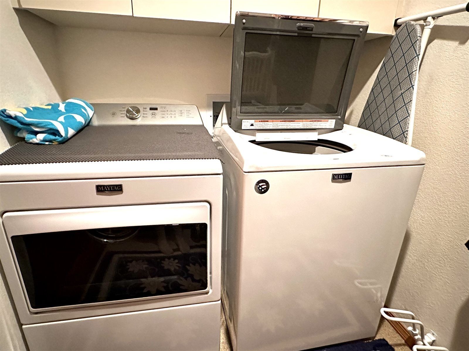 A compact laundry room with a front-loading washer, a stacked dryer, and a small window.