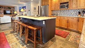Una cocina moderna con gabinetes de madera, una isla central con taburetes, un microondas integrado y un refrigerador grande.