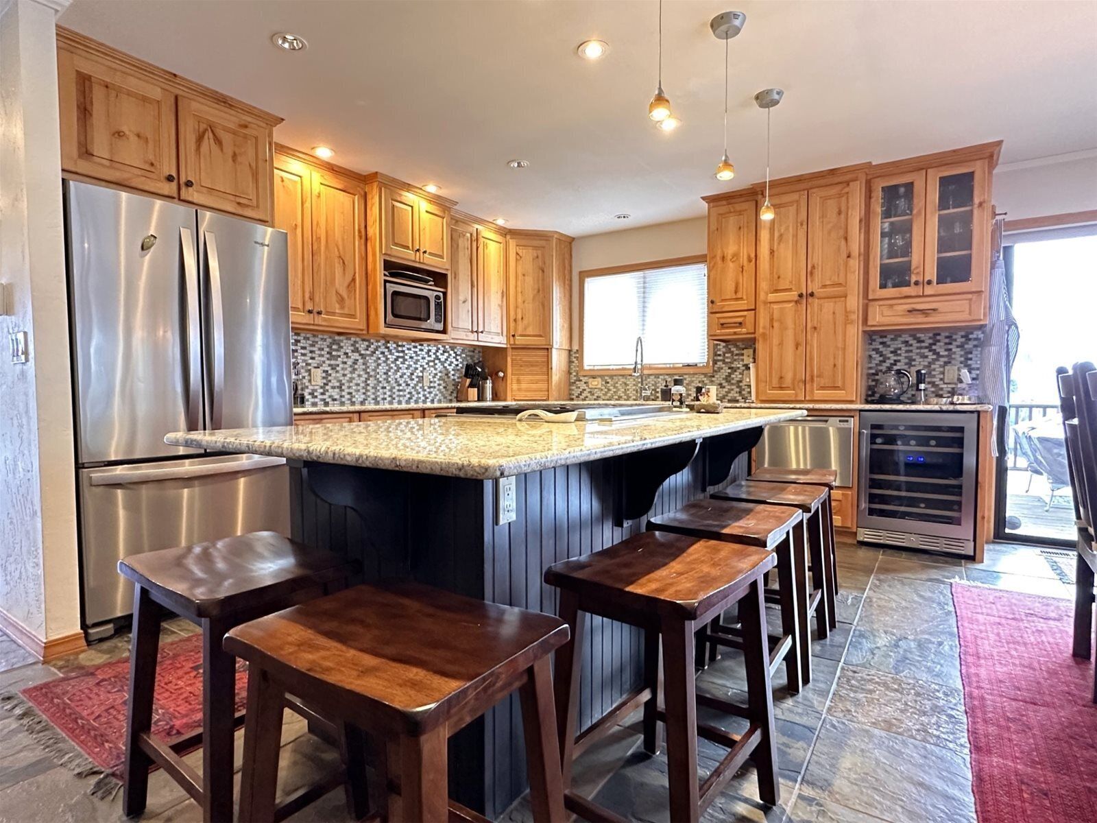 A modern kitchen with wooden cabinets, stainless steel appliances, a granite countertop, and bar stools.