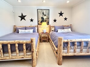 Une chambre à coucher avec deux lits en bois, une table de chevet avec une lampe, et des décorations murales comprenant des étoiles et un tableau représentant un ours.