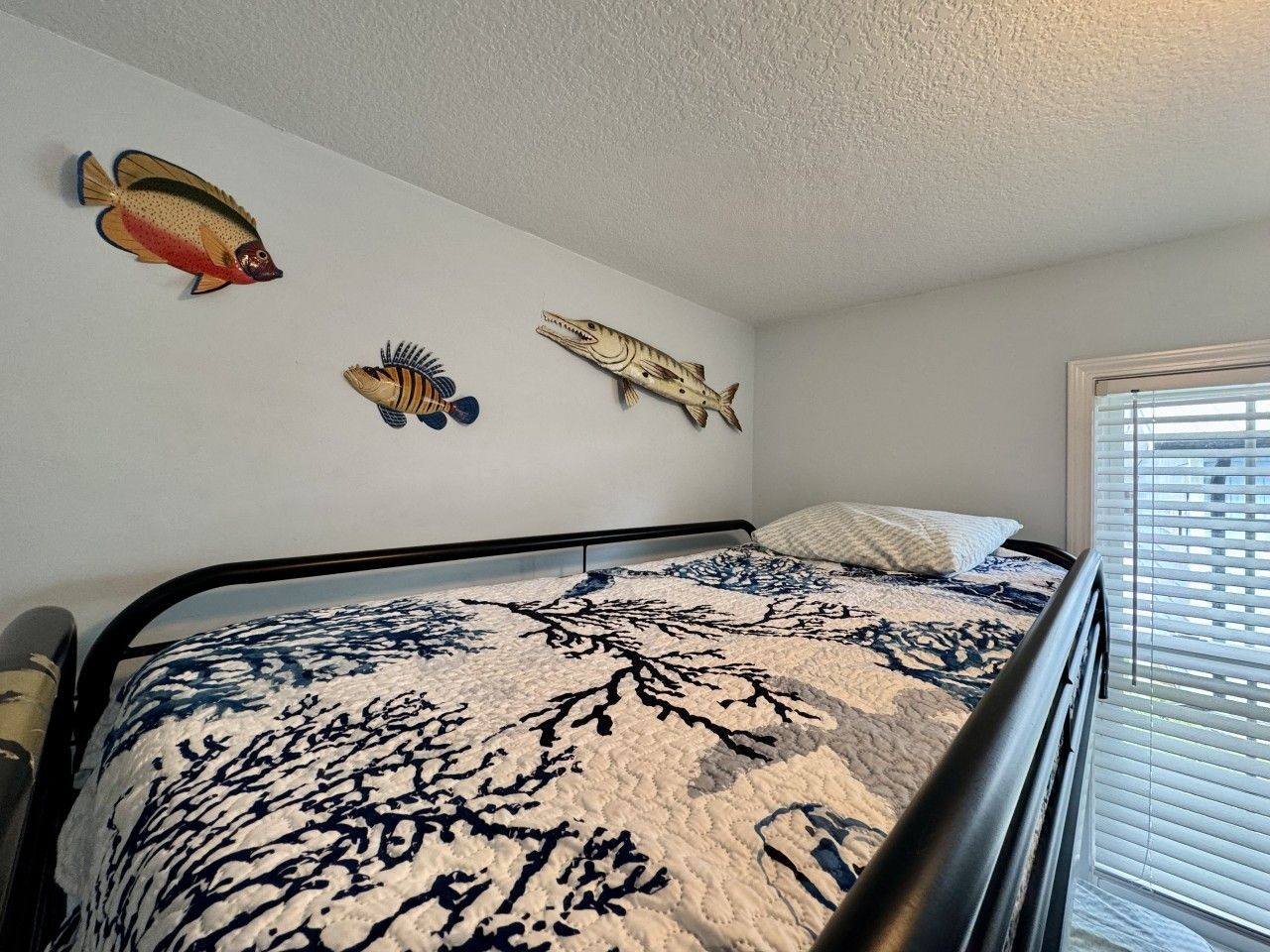Une chambre à coucher avec un lit, une fenêtre avec des stores et des décorations murales, notamment des motifs de poissons.