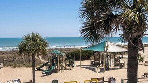 Une plage avec une aire de jeux, des palmiers et une vue dégagée sur l’océan.