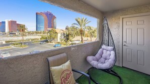 A balcony with a hanging chair, a door, and a view of a cityscape including tall buildings and palm trees.