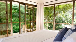 Una camera da letto con un letto grande, vista su un verde rigoglioso attraverso porte scorrevoli in vetro e un balcone con ringhiera rossa.