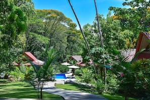 A lush garden with a pathway leading to a pool area, surrounded by tropical vegetation and traditional-style buildings with red roofs. - Royal Sabitha, Private Luxury Jungle Oasis w/pool & yoga deck! 5min from Surf! Dominical (Bahía Ballena)