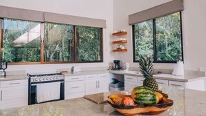 Una cucina moderna con ampie finestre, piano cottura a gas, mobili bianchi e una ciotola di frutta sul bancone.