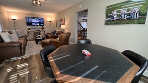 A living room with a brown leather sofa, a brown leather chair, a wooden dining table, and a television on the wall. - 7 mi to Grand Park, 1 mi to Mustard Seed, 5 min to downtown Noblesville! (Noblesville)