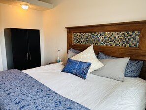 Una cama bien tendida con una colcha estampada, cabecera con diseño de mosaico y un armario negro.