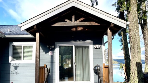 A wooden deck leading to a house with a covered porch, a sliding glass door, and a view of a lake. - The Mushroom Patch Cabin (Union)