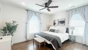 A bedroom with a bed, a ceiling fan, a bedside table with a lamp, and a window with curtains. - Beautiful 2BR Condo in Homewood next to SOHO (Birmingham)