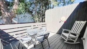 A wooden deck with a glass table and chairs, a rocking chair, and a white fence. - Beautiful 2BR Condo in Homewood next to SOHO (Birmingham)