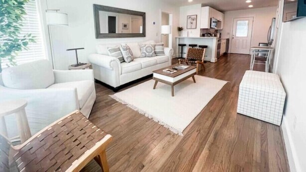 A modern living room with a white sofa, a wooden coffee table, and a dining area with a kitchen in the background. - Beautiful 2BR Condo in Homewood next to SOHO (Birmingham)