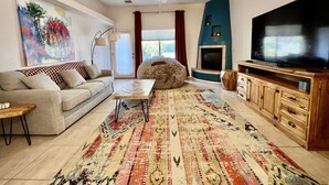 Un salon comprenant un canapé, une table basse, un téléviseur, une cheminée et un tapis coloré.