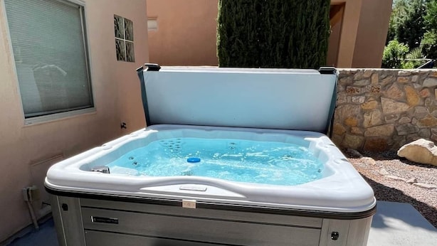 Un bain à remous avec des marches menant à celui-ci, installé sur une terrasse avec un mur en pierre et un grand arbre en arrière-plan.