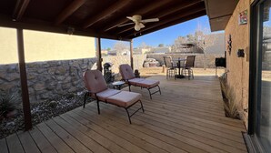 Un porche cubierto con piso de madera, dos sillas acolchadas, una mesa y un ventilador de techo.