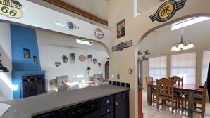 Una cocina con lavavajillas, un comedor con mesa y sillas de madera, y varios adornos en las paredes incluyendo logotipos y letreros.