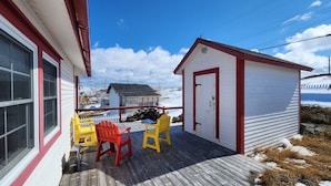 A wooden deck with two chairs, a small shed, and a view of a snowy landscape.