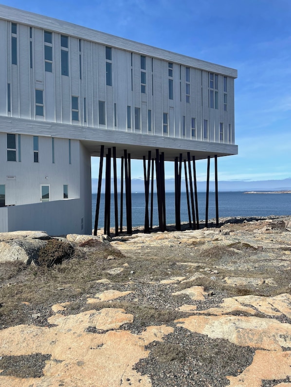 Un edificio moderno con techo plano sostenido por pilares verticales, situado en una costa rocosa con vistas al mar.