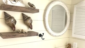 Une salle de bain avec un lavabo blanc, un meuble-lavabo en bois, des coquillages décoratifs, un miroir et une décoration maritime au mur.