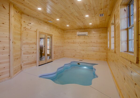 Ein Holzhütten-Interieur mit einem kleinen Pool, Holzwänden und einer Tür, die nach draußen führt.