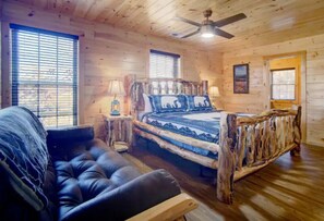Ein Schlafzimmer in einer Blockhütte mit einem hölzernen Bett, einem Ledersofa und einem Deckenventilator.