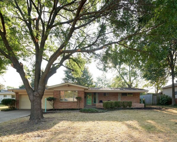 A single-story house with a brick exterior, a front porch, and a large tree in the yard. - Enjoy Mint: a fresh 1950s modern ranch style home (Tulsa)