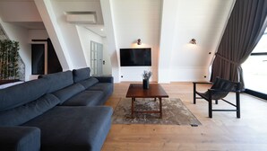 Ein modernes Wohnzimmer mit einem dunkelgrauen Ecksofa, einem Couchtisch aus Holz mit einer Vase und einem schwarzen Ledersessel.