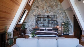 Ein Schlafzimmer mit schrägen Wänden, einer Steinwand, Holzbalken, einem Bett, Nachttischen und einem Fenster.