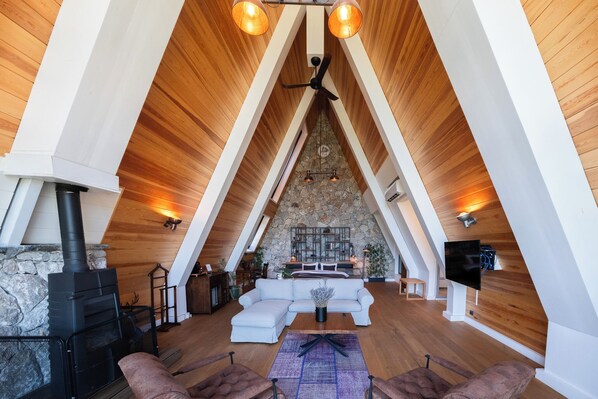 Un salón acogedor tipo loft con chimenea de piedra, vigas de madera y un sofá moderno.