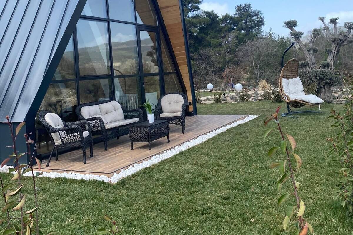 A modern house with a triangular roof, large glass windows, and a patio with outdoor furniture.