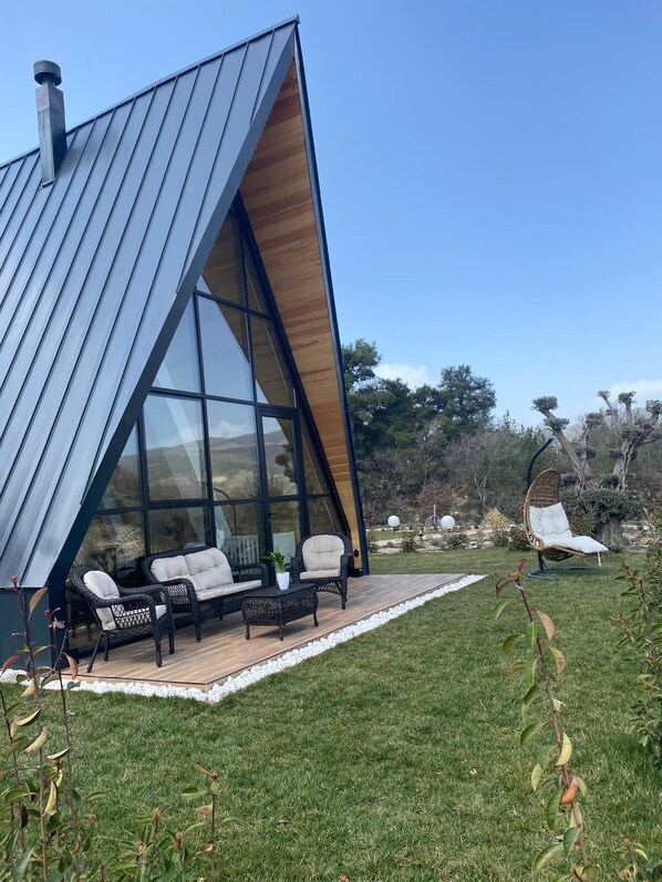 Una casa moderna con techo triangular, grandes ventanales y un patio con mobiliario exterior.