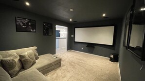 A home theater room with a dark wall, a large screen, a sofa, and a carpeted floor.