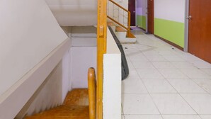 Una escalera de madera con barandilla, que conduce a un rellano con piso de baldosas.